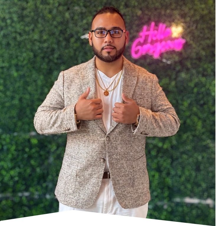 Aulundrew in a tan blazer in front of a green wall with a neon sign